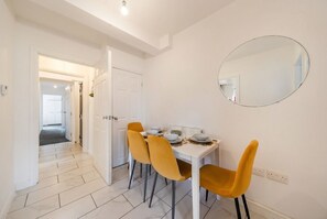 Ein Essbereich mit weißem Tisch, vier Stühlen und einem runden Spiegel an der Wand.