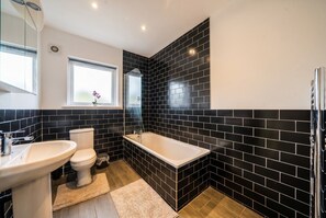 A bathroom with a bathtub, toilet, and sink, featuring black tiled walls and a wooden floor. - 5-Bed Flats Sleeping 11 · Free Parking · Near Beaumont Park, Huddersfield (Newsome)