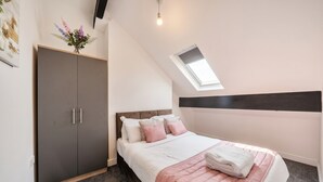 Una camera da letto con un letto, un armadio, un lucernario e una mensola a parete con fiori.