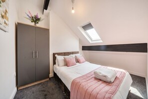 Ein Schlafzimmer mit Bett, Schrank, Dachfenster und einer Wandablage mit Blumen.