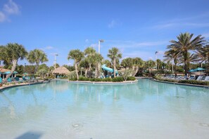 A resort pool with palm trees, lounge chairs, and a water slide. - Disney Themed Condo- Championsgate Resort (Kissimmee)