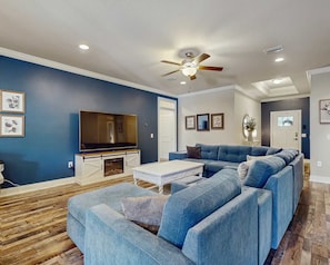 A living room with a sectional sofa, a flat-screen TV, a ceiling fan, and a fireplace. - Pet-friendly 3-bed pool home near Destin & Pensacola beaches, seafood, & fun! (Navarre)