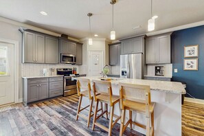 A modern kitchen with grey cabinets, stainless steel appliances, a central island with bar stools, and a patterned floor. - Pet-friendly 3-bed pool home near Destin & Pensacola beaches, seafood, & fun! (Navarre)