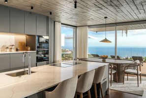A modern kitchen with a large island, a dining area with a view of the sea, and a balcony with outdoor seating. - Casa Mareva – Above the Atlantic (Calheta)