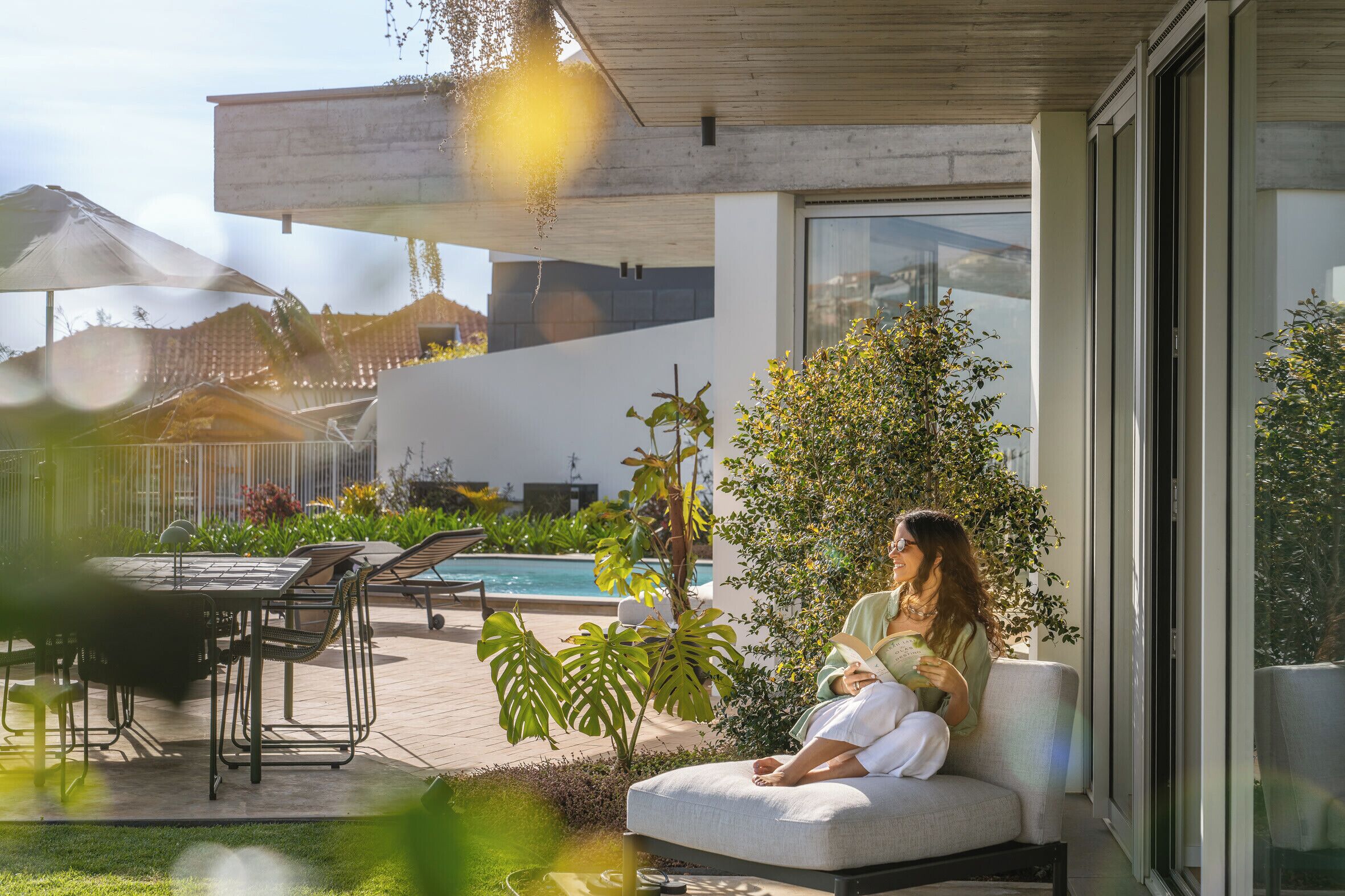 Een modern terras buiten met een zwembad, lounge stoelen en een eettafel.