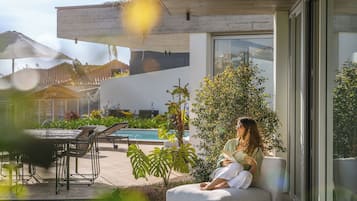Een modern terras buiten met een zwembad, lounge stoelen en een eettafel.