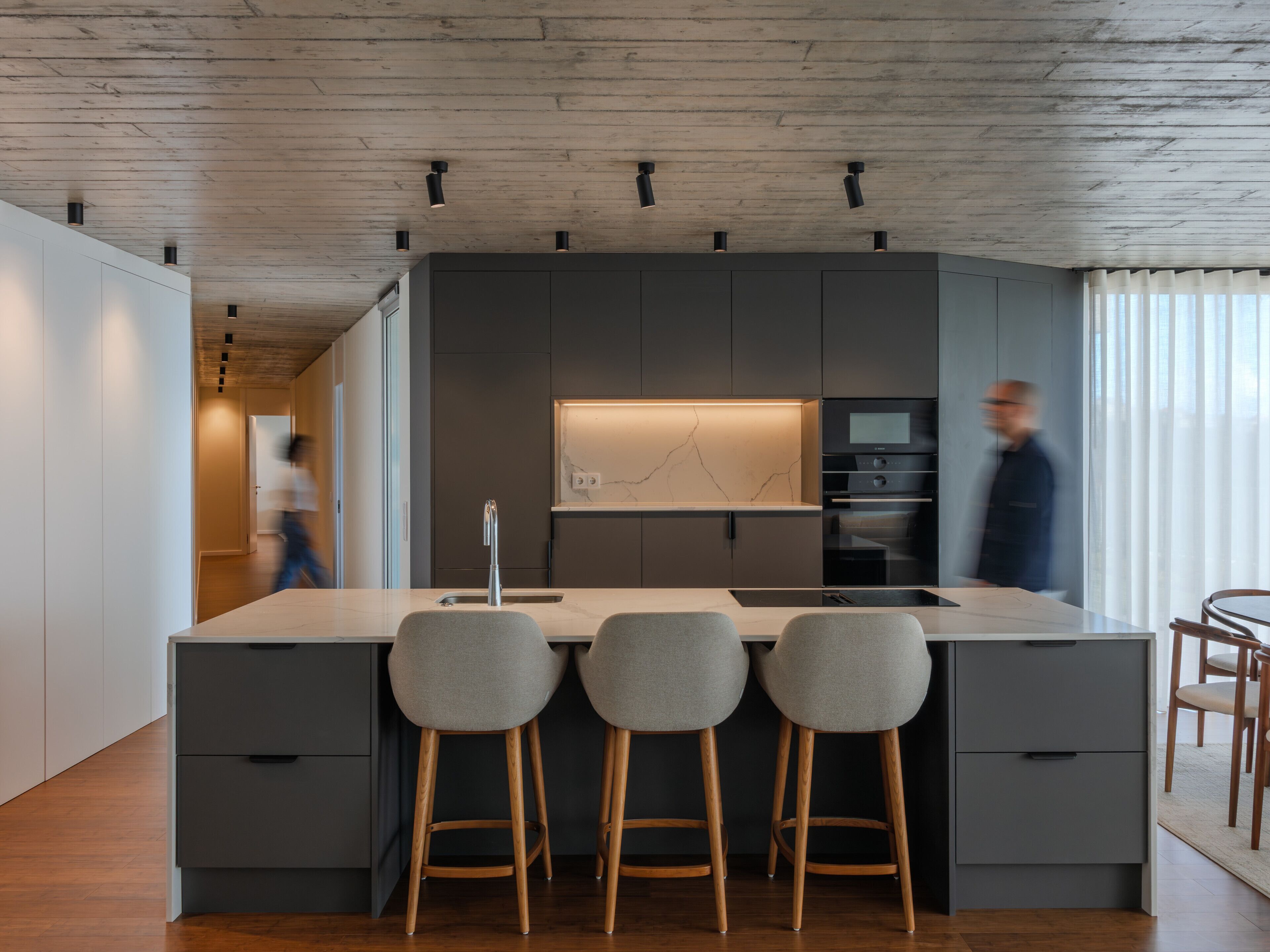 Une cuisine moderne dotée d’un îlot central, de tabourets de bar et d’appareils électroménagers intégrés.