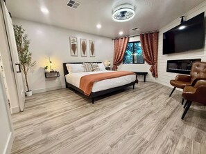 Ein modernes Schlafzimmer mit einem Bett, einem Fernseher, einer Bank und einem Sessel.