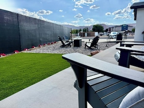An outdoor patio area with a lawn, seating, and a view of a parking lot and buildings in the background. - Located in Downtown Kanab I All-New Home! (Kanab)
