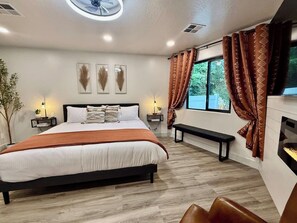 Un dormitorio moderno con una cama grande, mesitas de noche, un banco y vistas al exterior.