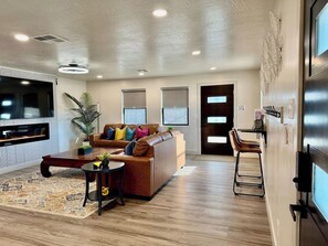 A modern living room with a brown leather sofa, a coffee table, and a TV mounted on the wall. - Located in Downtown Kanab I All-New Home! (Kanab)