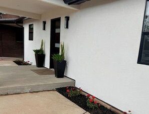 Ein modernes Gebäude mit Betonfassade, Blumentöpfen und einem kleinen Blumenbeet.