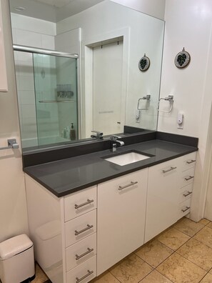 Ein modernes Badezimmer mit großem Spiegel, Waschbecken und einer Duschkabine aus Glas.