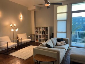 Ein modernes Wohnzimmer mit einer Couch, Sesseln, einem Couchtisch, einem Bücherregal und einem Deckenventilator.