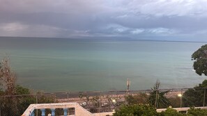 Vista sulla costa con cielo sereno, mare calmo e un'area recintata con una panchina.