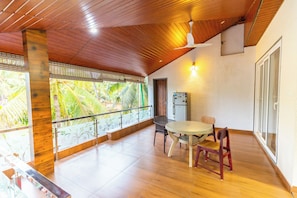 A spacious balcony with a wooden ceiling, a table with chairs, and a view of palm trees.