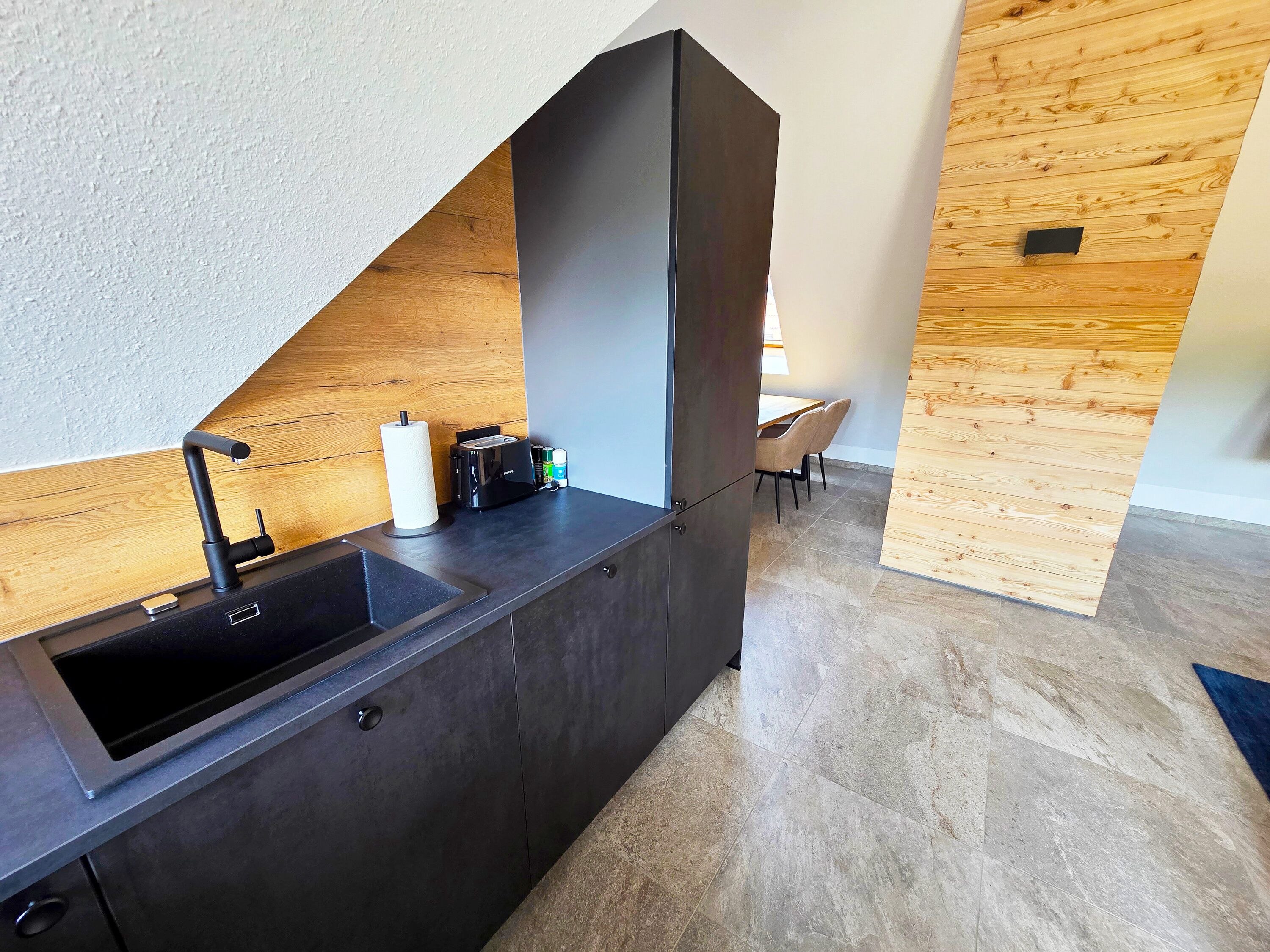 Una cocina moderna con pileta integrada, un revestimiento de pared de madera y un comedor con sillas.