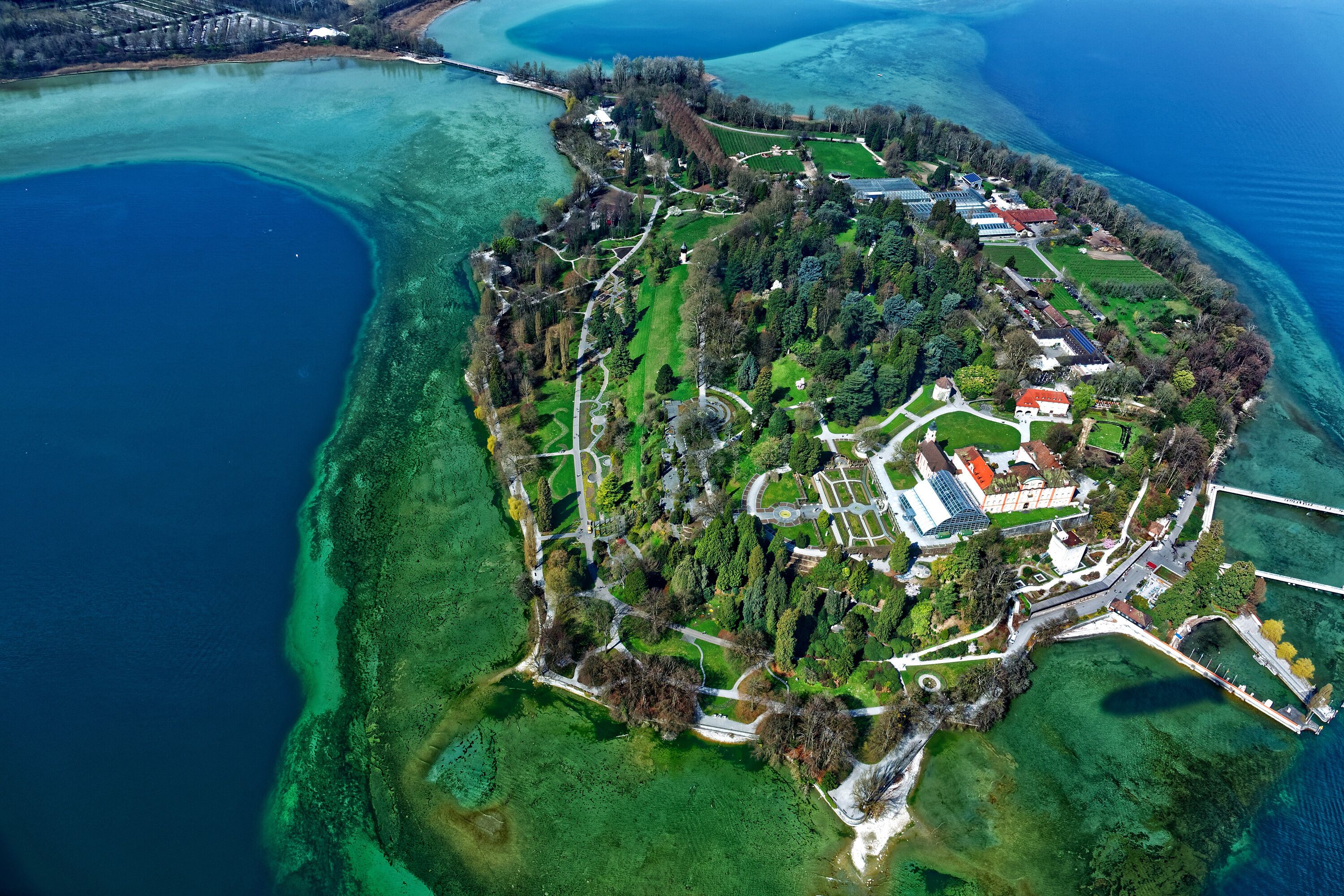 Vue aérienne d’une propriété située sur la côte, avec un bâtiment principal entouré d’espaces verts et d’un port de plaisance.