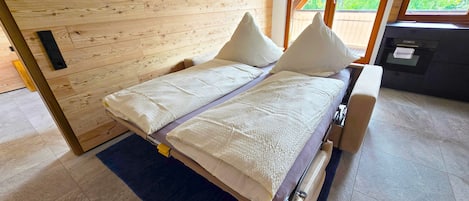 Un lit avec une tête de lit en bois, un tapis bleu et une vue sur l’extérieur par une fenêtre.