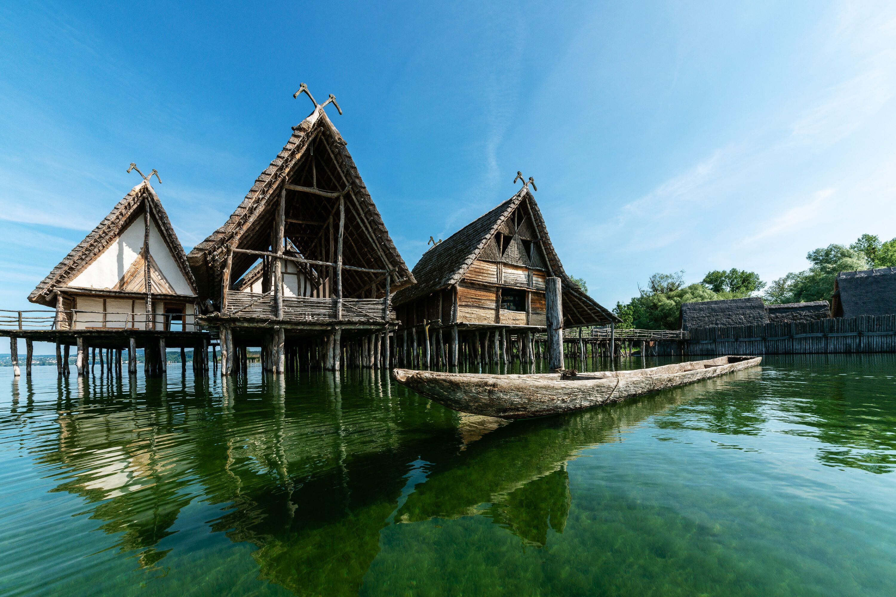 A traditional wooden house with a thatched roof, built on stilts over water.