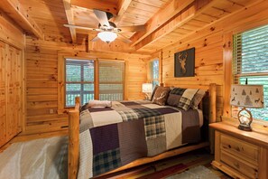 A wooden cabin bedroom with a bed, nightstands, a ceiling fan, and a window with blinds. - Elevated Smoky Mountain Escape l 4,800' Views, Hot Tub & Sauna l Blue Ridge Mtn (Maggie Valley)