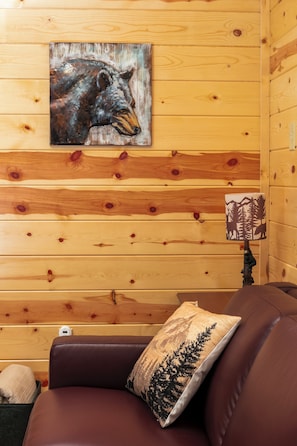 Ein Holzblockhaus-Interieur mit einem braunen Ledersofa, einem Zierkissen, einer Wandleuchte und einem Bärenbild.