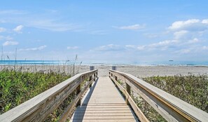 A wooden boardwalk leading to a beach with a ship in the distance. - Beachfront 3BR Main Floor Condo/ Steps to Beach (Cocoa Beach)