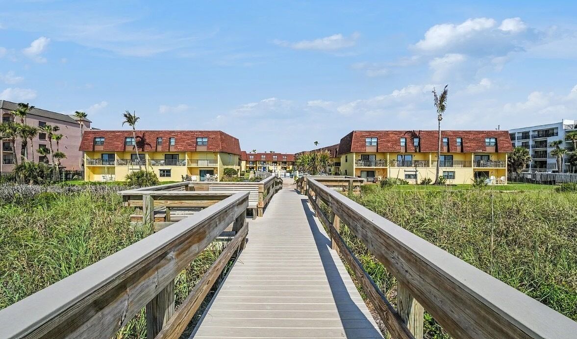 A wooden boardwalk leading to a row of yellow buildings with red roofs.