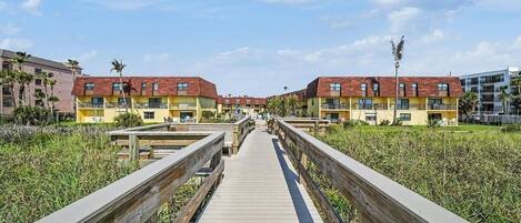 A wooden boardwalk leading to a row of yellow buildings with red roofs.