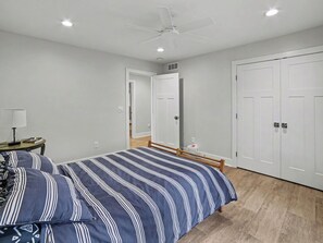 Quarto com cama, mesa de cabeceira, luminária, ventoinha de teto e guarda-roupa.