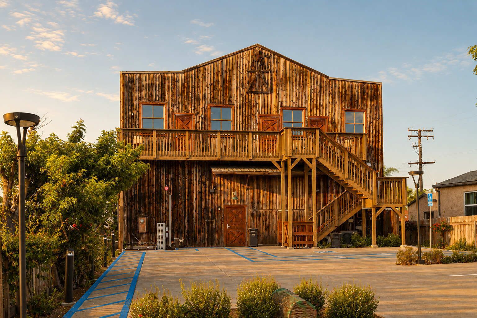 A rustic wooden building with a balcony, a staircase, and a parking lot with blue lines.