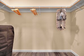 Een kamer met een droogrek aan het plafond, een strijkplankstation aan de muur en een bruine bank.