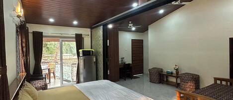 Une chambre spacieuse comprenant un lit, un coin salon avec un canapé, un ventilateur de plafond et un réfrigérateur.