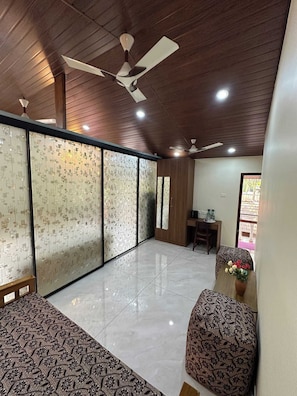 A spacious room with a high ceiling, a ceiling fan, and a dining area with a table and chairs. - Cornelio Residence - 1 BR studio with AC in Udupi (Padutonse)