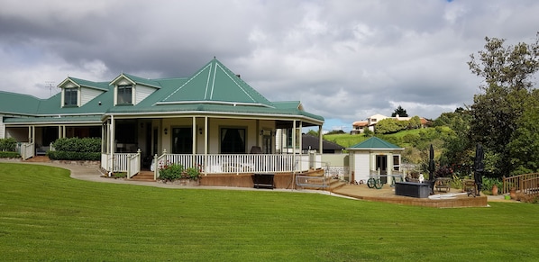 A large house with a green roof, a covered porch, and a well-maintained lawn.