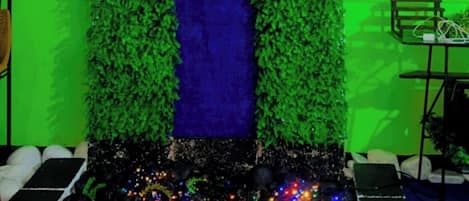Una entrada decorada con un cartel que dice '¡Feliz 28 cumpleaños, Nick!', follaje verde y una fuente con caída de agua azul.
