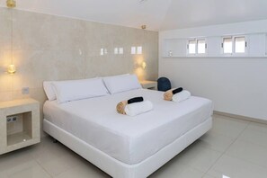 A modern hotel room with a large bed, two bedside tables, a built-in shelf, and a window with blinds. - 6-Bedroom Luxury Villa | Pool, Hot Tub, Movie Theater & Pool Table (Adeje)