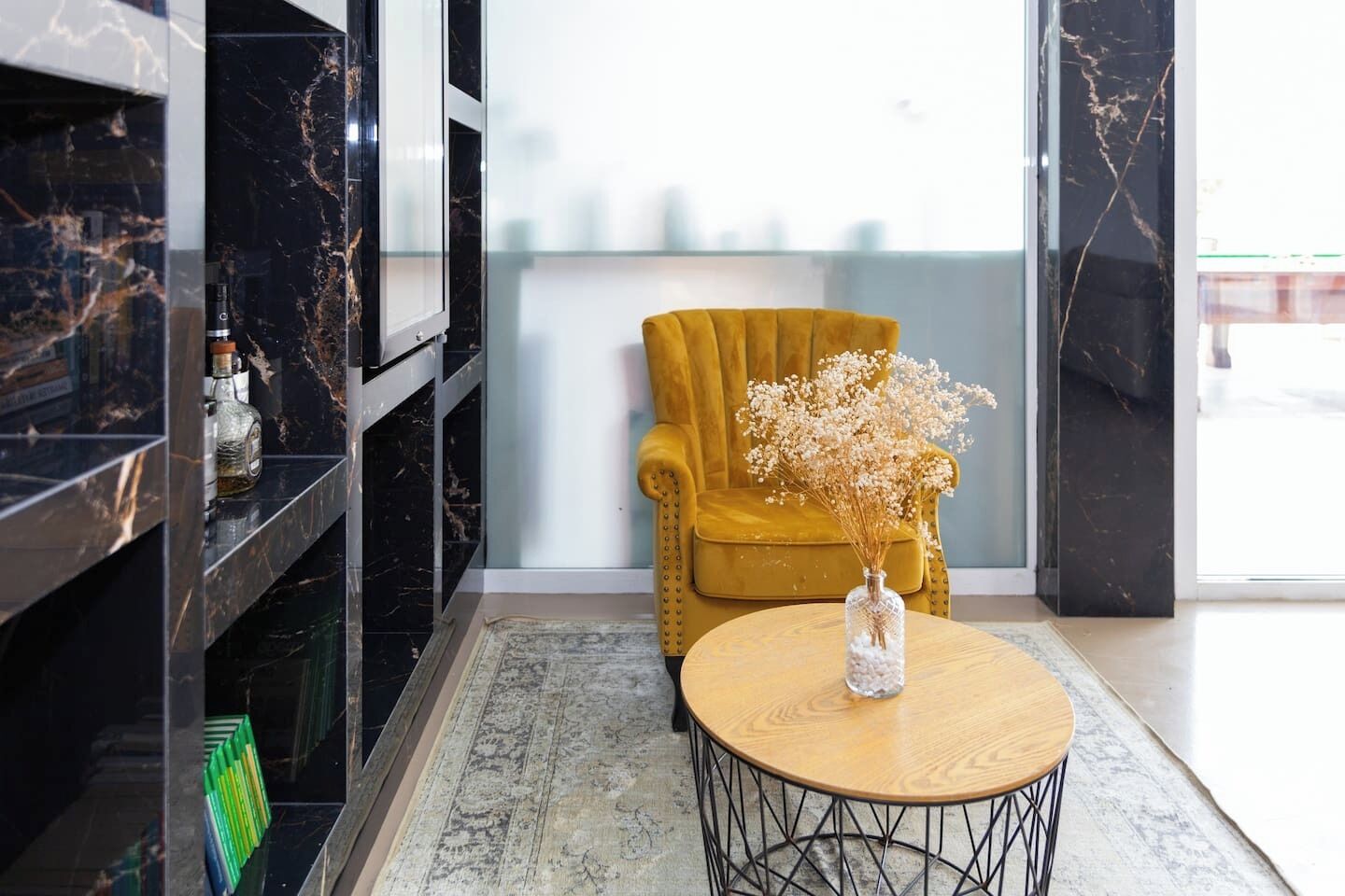A modern interior with a yellow armchair, a round wooden table with a glass vase, and a black marble wall.