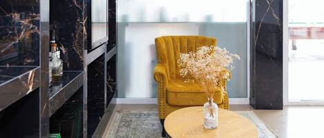 A modern interior with a yellow armchair, a round wooden table with a glass vase, and a black marble wall.