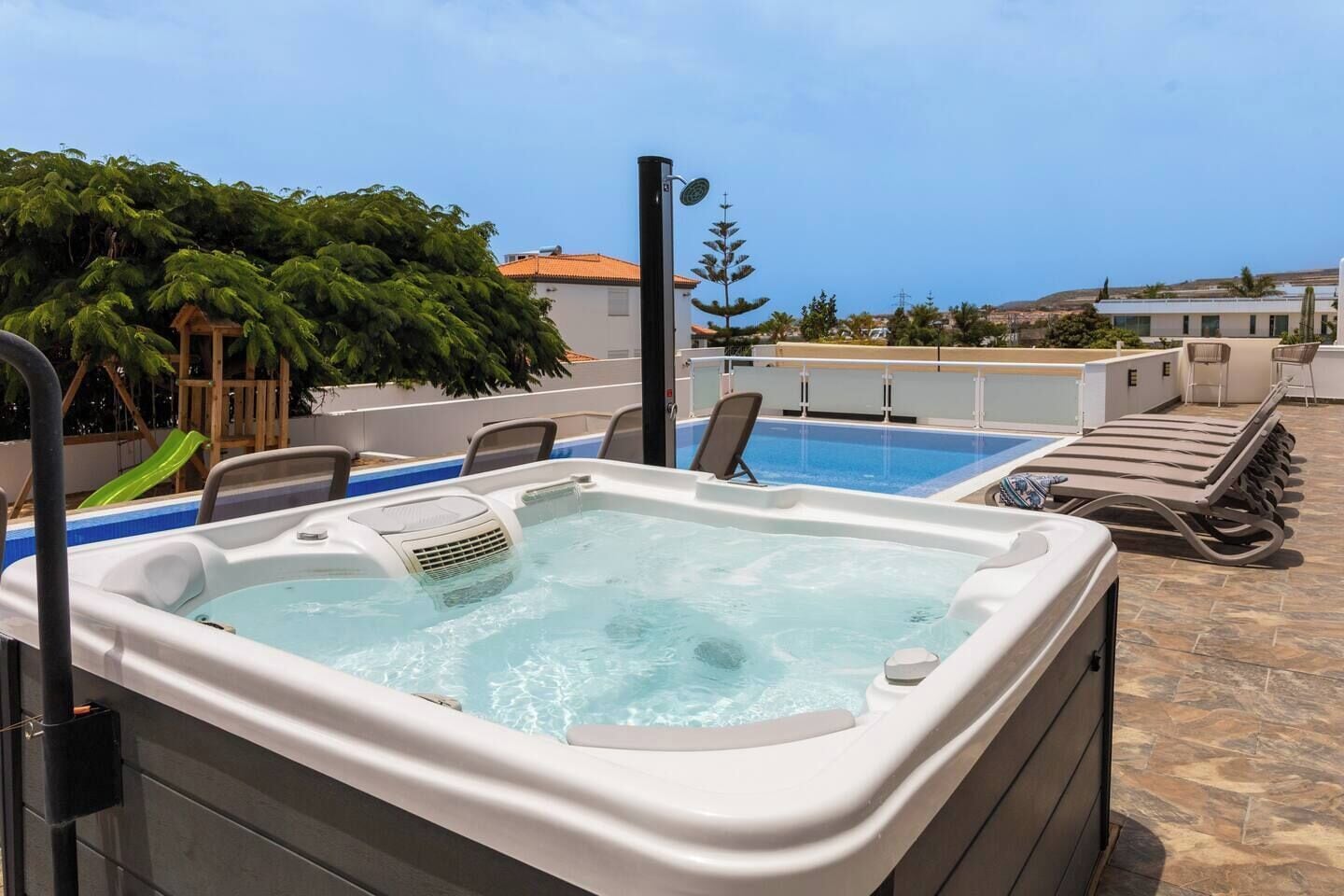 A rooftop pool area with a hot tub, lounge chairs, and a view of the sea.