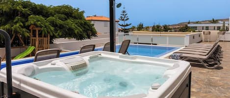 Uma área de piscina no terraço com hidromassagem, espreguiçadeiras e vista para o mar.