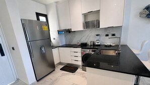 A modern kitchen with a stainless steel refrigerator, a black countertop, white cabinets, and a built-in microwave. - Apartamento con balcon en Cana Bay Punta Cana (Punta Cana 23000)