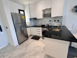 Uma cozinha moderna com geladeira de aço inoxidável, bancada preta, armários brancos e micro-ondas embutido.