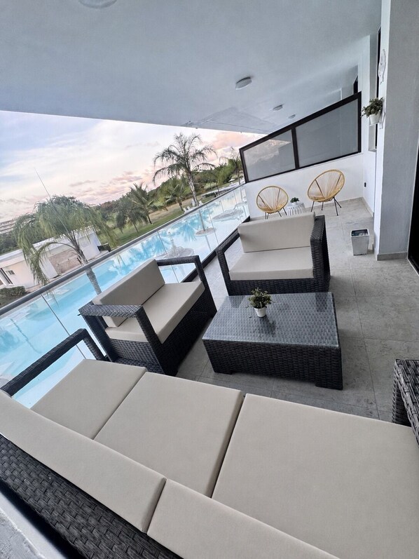 Ein moderner Außenbereich mit Liegebereich, Pool, Korbmöbeln und Blick auf Palmen.
