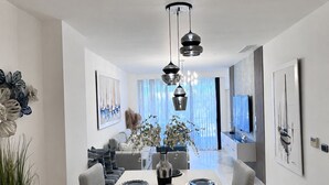 A modern dining area with a central table, chairs, and a chandelier. - Apartamento con balcon en Cana Bay Punta Cana (Punta Cana 23000)
