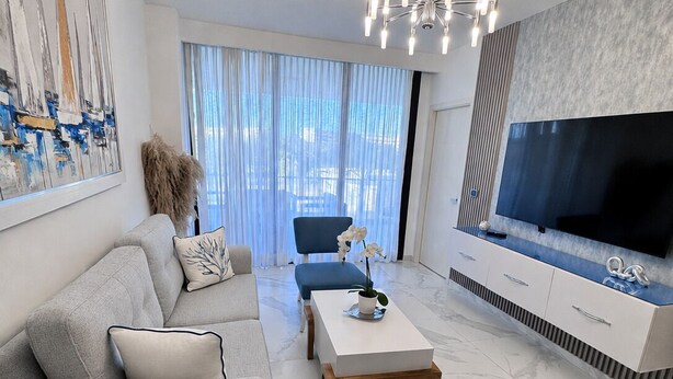 A modern living room with a sofa, ottoman, coffee table, and a TV on a stand. - Apartamento con balcon en Cana Bay Punta Cana (Punta Cana 23000)