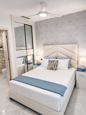 Ein modernes Schlafzimmer mit einem großen Bett, einem Deckenventilator und einem Badezimmer mit Toilette und Waschbecken.