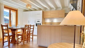 A modern kitchen with wooden cabinets, a central island, and a dining area with a round table and chairs. - Heart of Les Gets - Apartment for 6 people - 3 bedrooms (Les Gets)