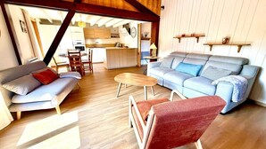 A cozy living room with a sofa, armchair, and coffee table, wooden flooring, and a kitchen in the background. - Heart of Les Gets - Apartment for 6 people - 3 bedrooms (Les Gets)