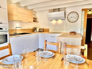 A modern kitchen with white cabinets, a wooden dining table set with plates, glasses, and cutlery.